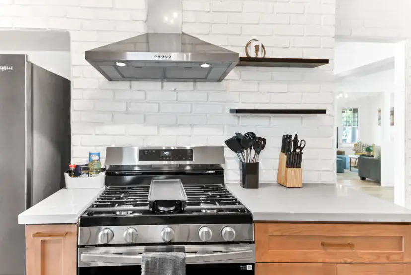 Gas range with a steel hood on white brick