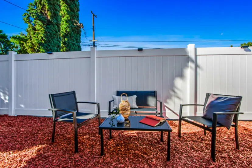 Patio seating on red mulch beside a white fence