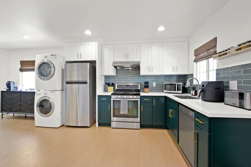 Kitchen with deep green cabinets, a blue tile backsplash and a stacked washer and dryer