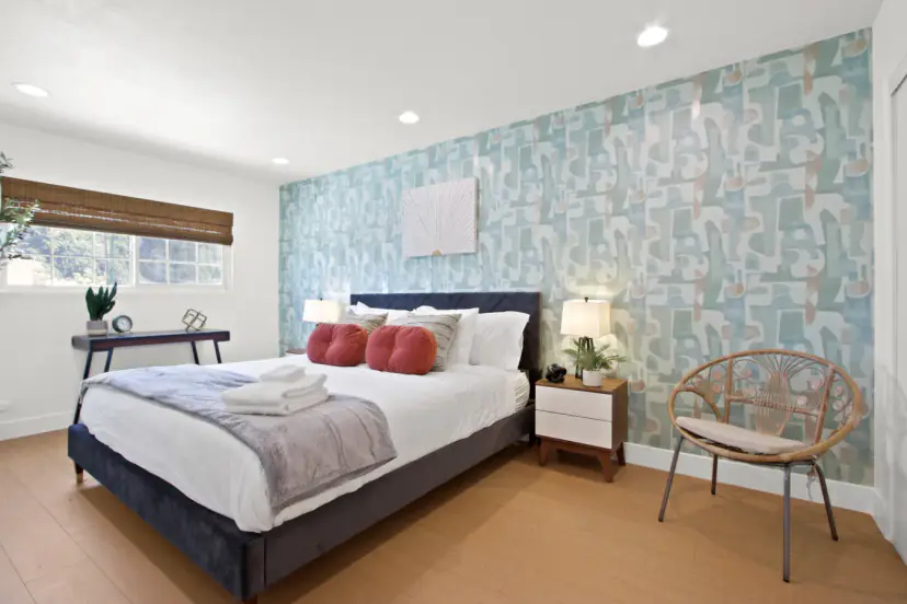 Bedroom with a patterned wallpaper wall, a velvet bed and a rattan chair