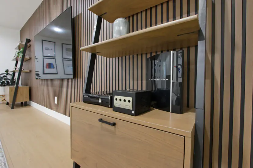 Retro game consoles on a cabinet beside the TV wall