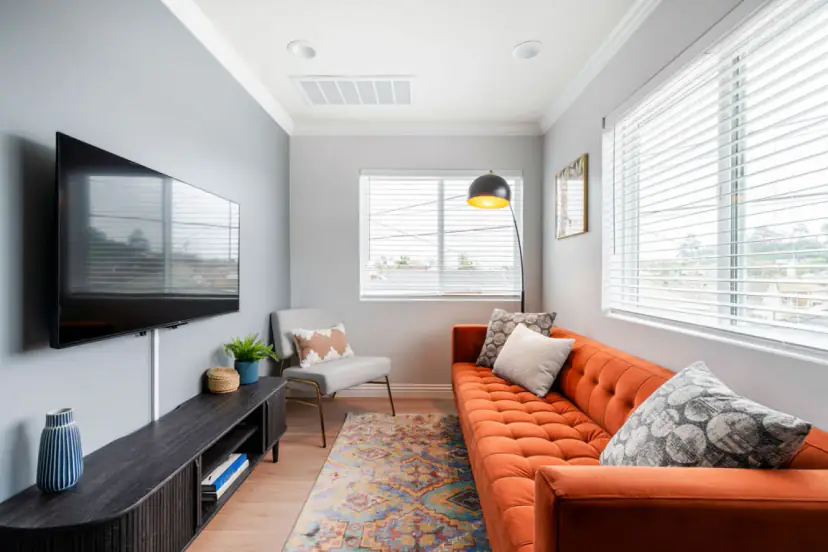 Living room with a burnt-orange tufted sofa, a wall-mounted TV and a patterned rug