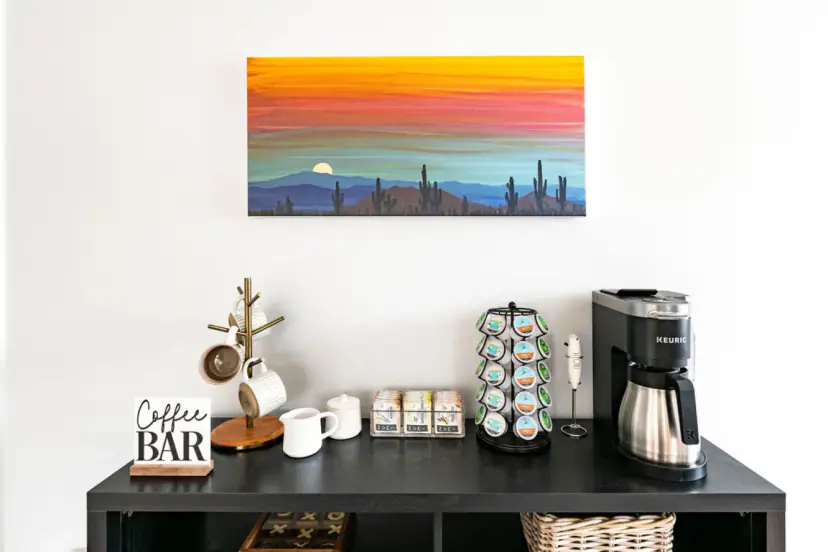 Coffee bar with a pod coffee maker under a desert sunset painting