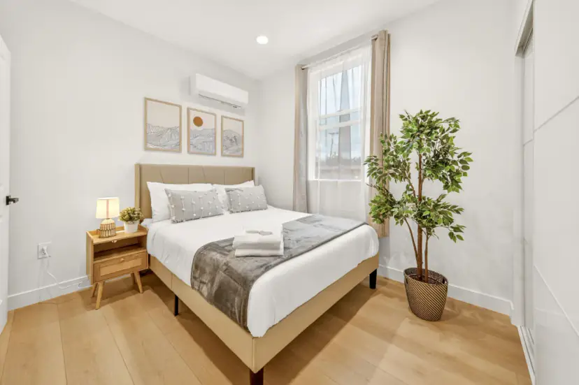 Bedroom with an upholstered bed, a potted tree and a wall air conditioner