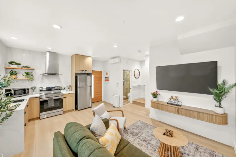 Open living room and kitchen with a wall-mounted TV and a fluted wood console