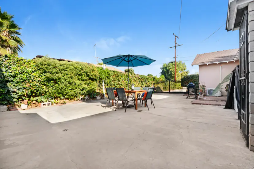 Paved backyard with an umbrella table, a grill and a gate