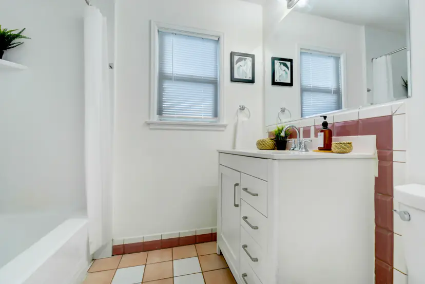 Bathroom with a tub, a white vanity and rose tile accents