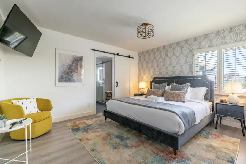 Main bedroom with a king bed, a yellow chair, a wall TV and a barn door to the bathroom