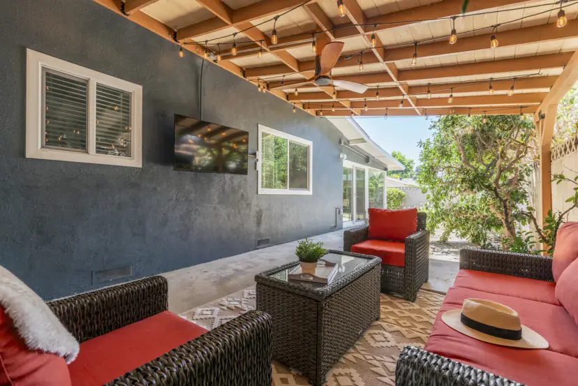 Covered patio with string lights, an outdoor TV and red-cushioned wicker sofas