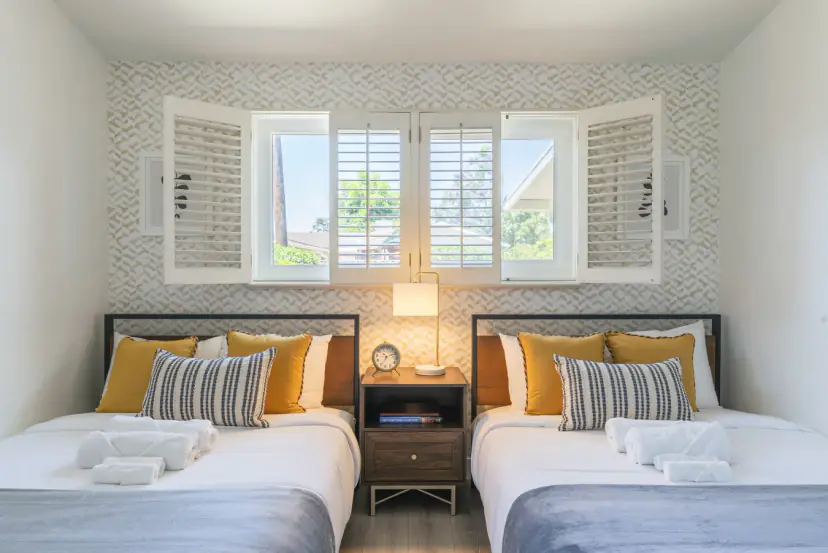 Twin room with mustard pillows under shuttered windows