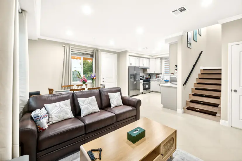 Living room with a leather sofa, dining area, kitchen and stairs