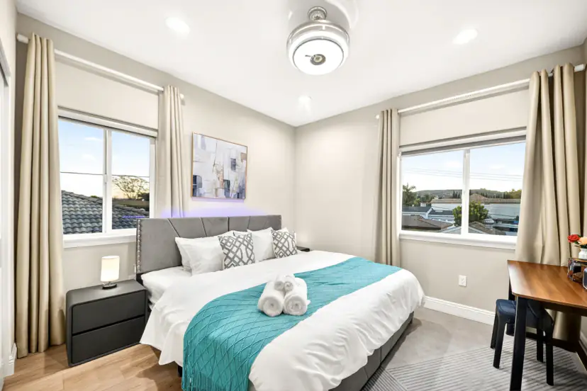 Upstairs bedroom with windows on two sides, a desk and teal throw