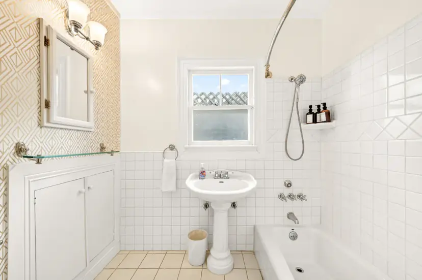 Classic white-tile bathroom with a pedestal sink and tub