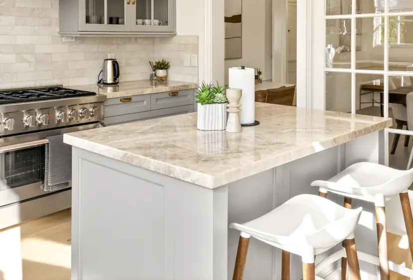 Kitchen island with a quartzite counter, white stools and a gas range