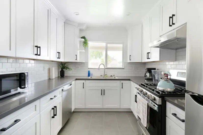 White kitchen with grey counters, a dishwasher and a window over the sink