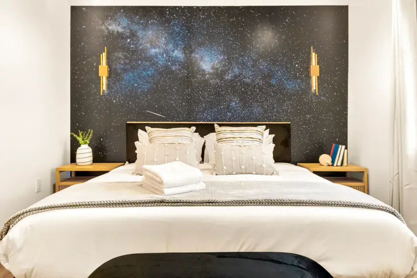 Bedroom with a Milky Way accent wall, gold sconces and a king bed
