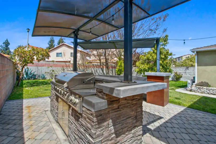 Built-in outdoor kitchen with a grill under a shade canopy